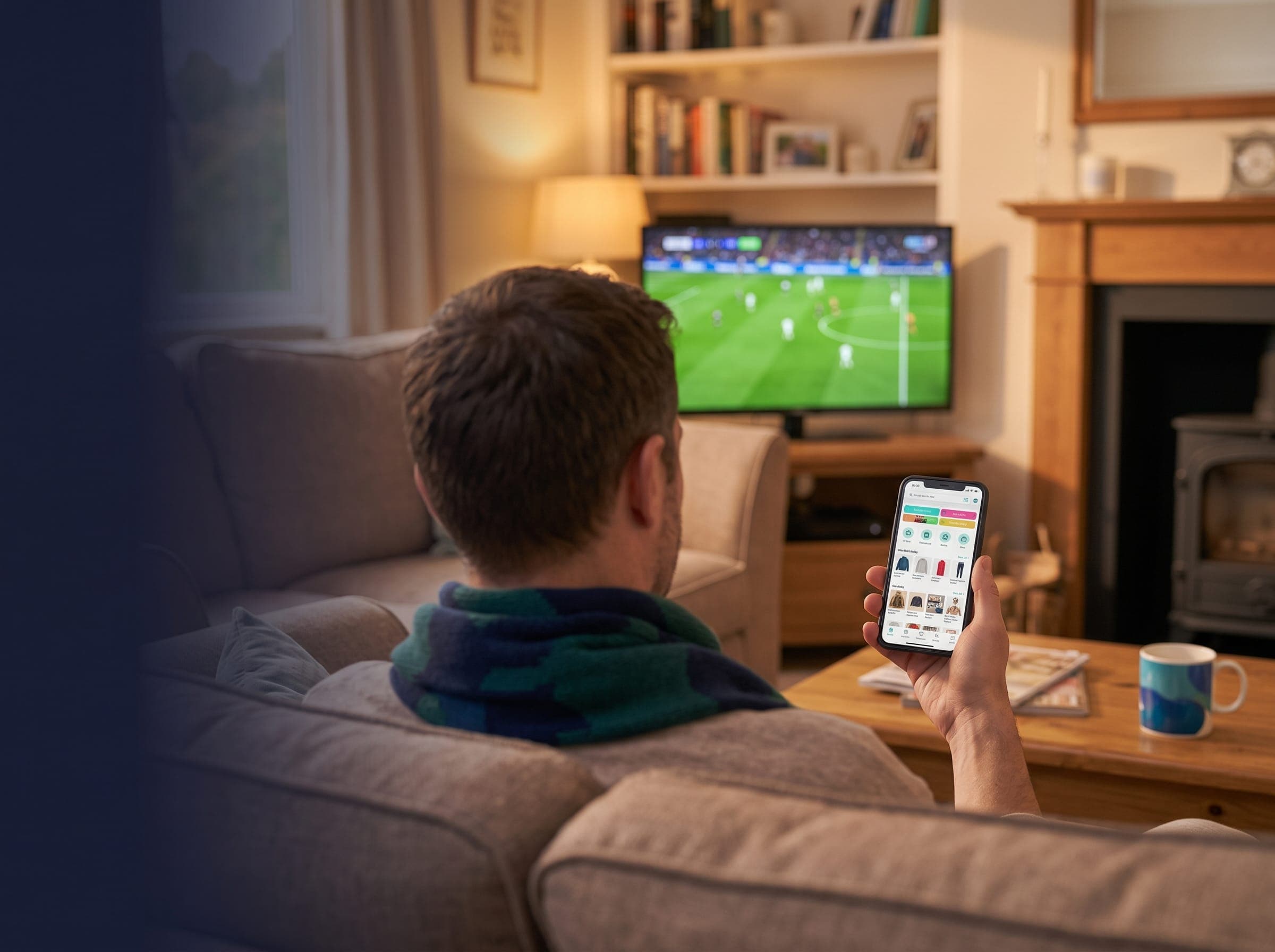 A supporter on the sofa at home, shopping on his phone with the match on TV